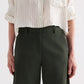 A person wears TWP's Slouchy BF Cotton Linen Twill Trouser in dark green, paired with a cream-striped button-up shirt, shown from shoulders to knees with arms relaxed at their sides.