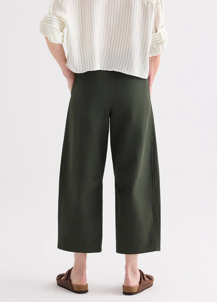Person seen from behind wearing a white striped shirt, TWP Slouchy BF Cotton Linen Twill Trouser in dark green, and brown sandals.