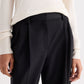 A person wearing a cream long-sleeve ribbed top tucked into the TWP Ivy Pant—high-waisted black Italian wool twill pleated trousers—shown from mid-torso to upper thighs.