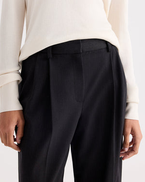 A person wearing a cream ribbed long-sleeve top and TWP’s Ivy Italian Wool Twill Pant—a mid-rise, pleated trouser in luxurious Smoke wool twill—shown from waist to mid-thigh.