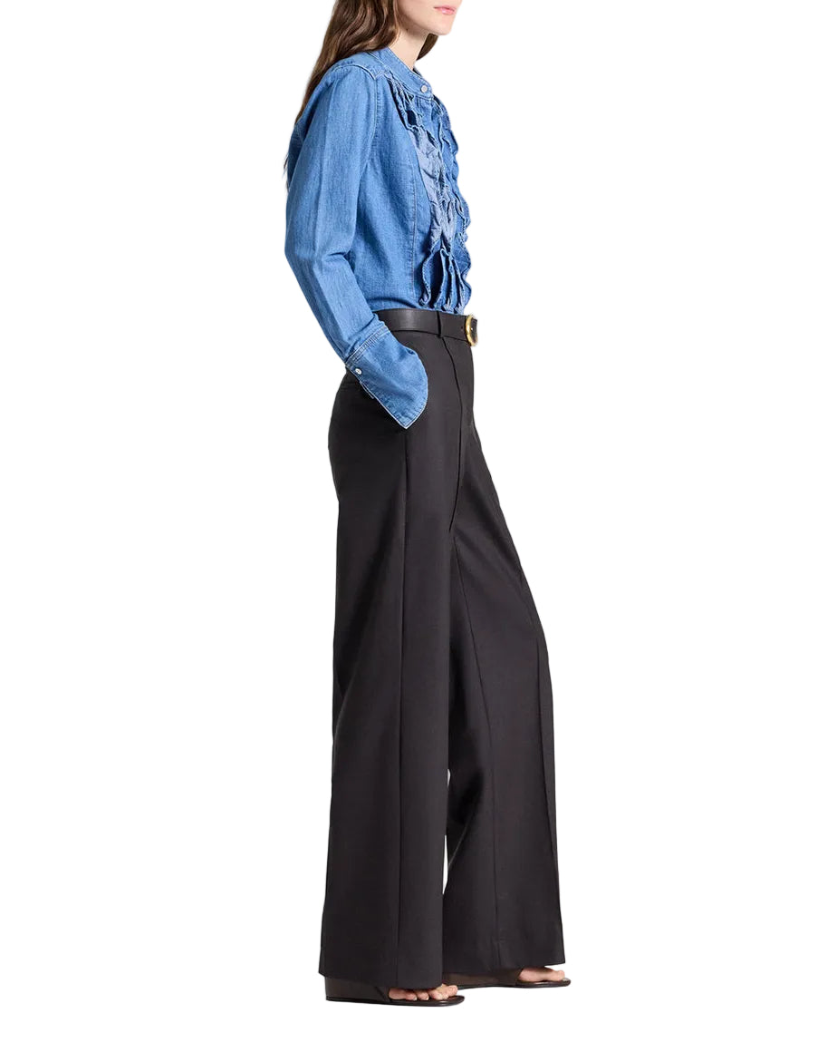 Person in profile wearing a blue ruffled blouse tucked into TWP Isla Pant mid-rise, wide-leg trousers with black heeled sandals.
