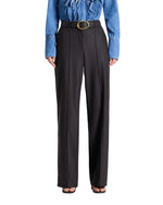 Person wearing TWP Isla Pant, high-waisted wide-leg black trousers with a wide belt, and a blue button-up shirt, standing facing forward.