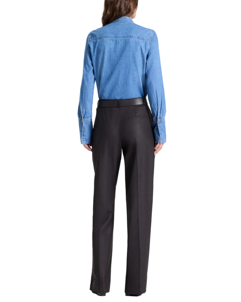 Person facing away in a blue denim shirt tucked into TWP Isla Pant, black mid-rise wide-leg trousers, against a white background.
