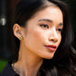 A woman with long dark hair wears Juliska Capucine De Wulf Berry Clover Convertible Duo Earrings and a black top, looking to the side outdoors.