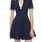 A woman models the Simkhai Page Knit Polo Mini Dress, featuring short sleeves, navy blue knit fabric, a white collar, and white sleeve trim, set against a plain background.