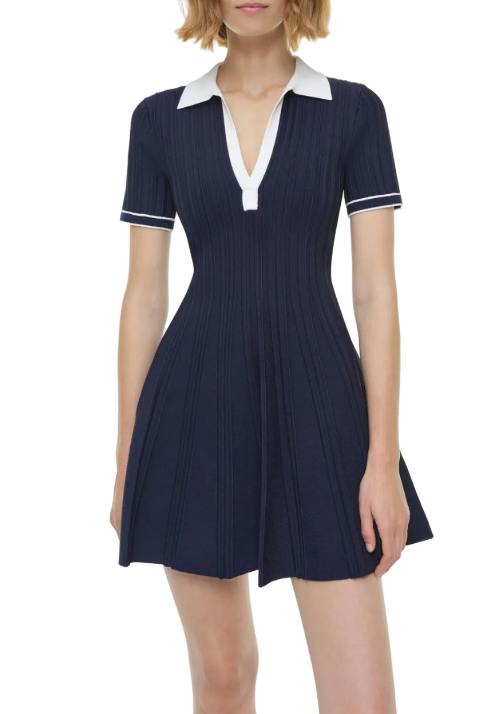 A woman models the Simkhai Page Knit Polo Mini Dress, featuring short sleeves, navy blue knit fabric, a white collar, and white sleeve trim, set against a plain background.