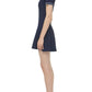 A woman stands in profile wearing the Simkhai Page Knit Polo Mini Dress in navy with a white collar and trim, short sleeves, and white heeled sandals.