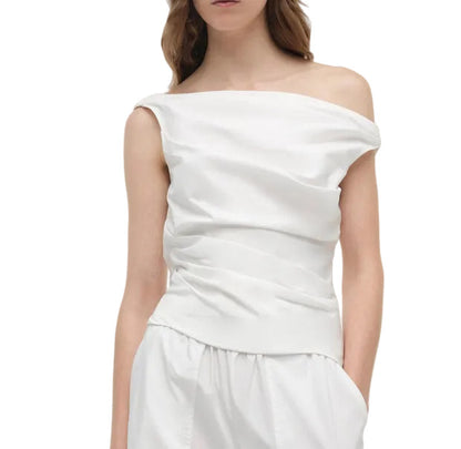 A woman models the Simkhai Maisel Draped Top with an off-the-shoulder design, paired with matching white pants, set against a plain white background.