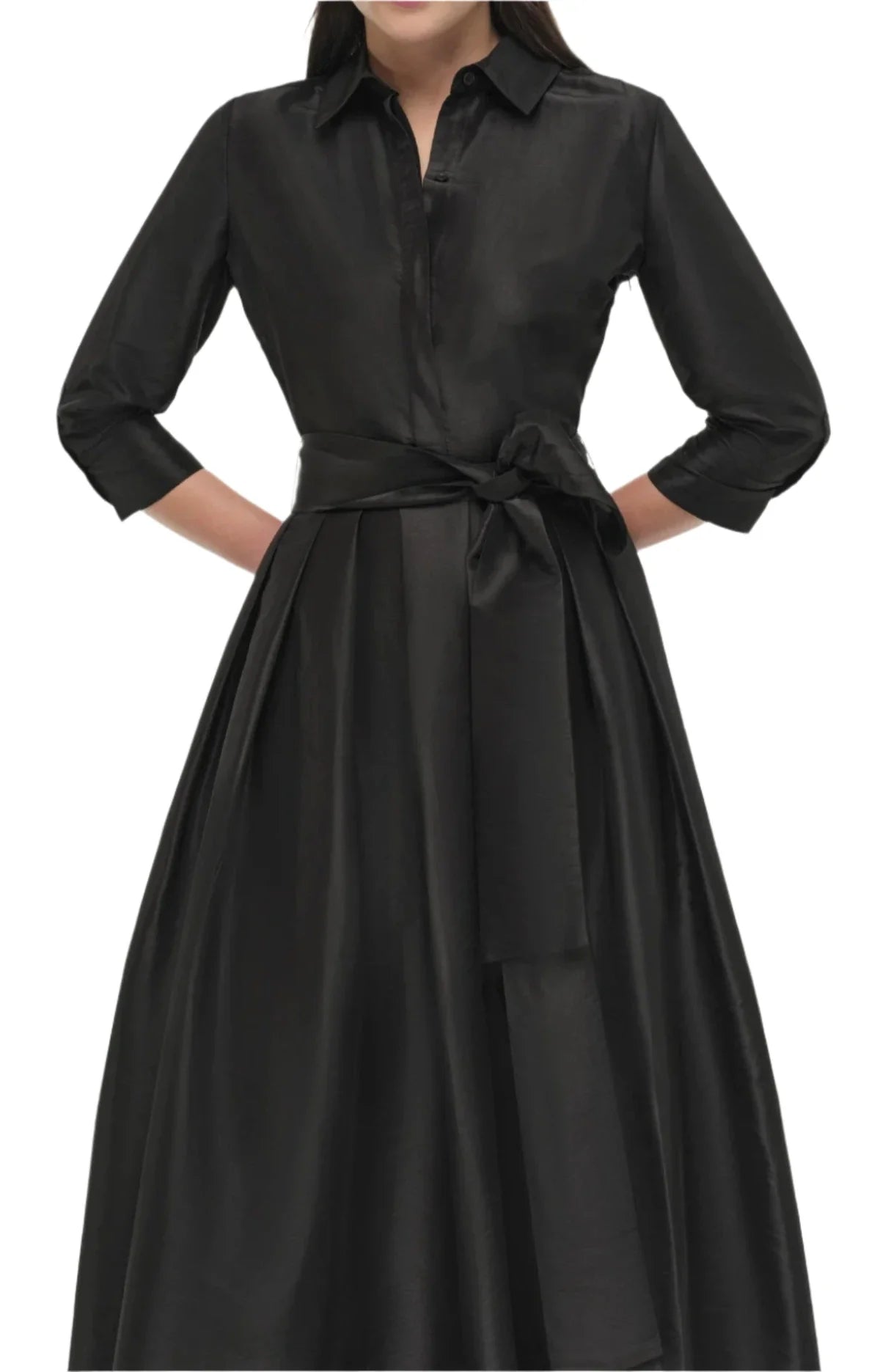 A woman is wearing the Simkhai Julip Belted Gown, a long-sleeve black satin dress from Simkhai, featuring tailored details with a collared neckline and a sash tied at the waist. She is visible from shoulders to mid-calf.