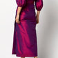A person wearing the Ann Mashburn Kira Silk Shantung Wrap Skirt in shiny magenta, paired with black high-heeled sandals, shown from the back against a plain background.