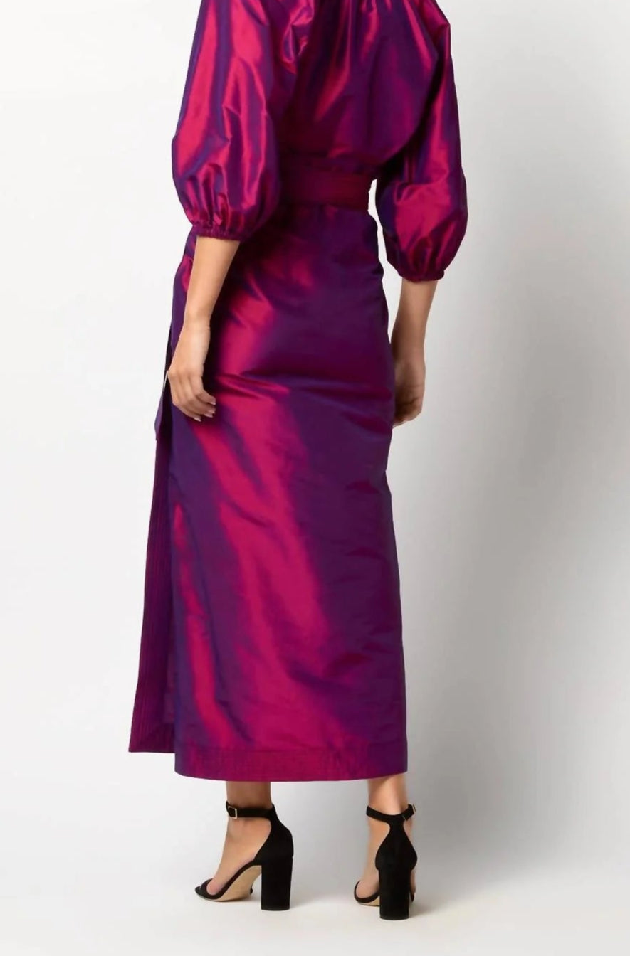 A person wearing the Ann Mashburn Kira Silk Shantung Wrap Skirt in shiny magenta, paired with black high-heeled sandals, shown from the back against a plain background.