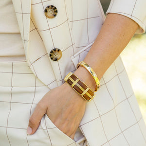 A person wearing a cream checkered suit with one hand in their pocket, showcasing two gold bracelets and the Juliska Capucine De Wulf Gaia Hinged Bangle on their wrist.