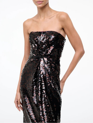 A woman wearing the Staud Cece Dress, a sequined strapless style featuring a subtle belt detail, stands against a plain white background.