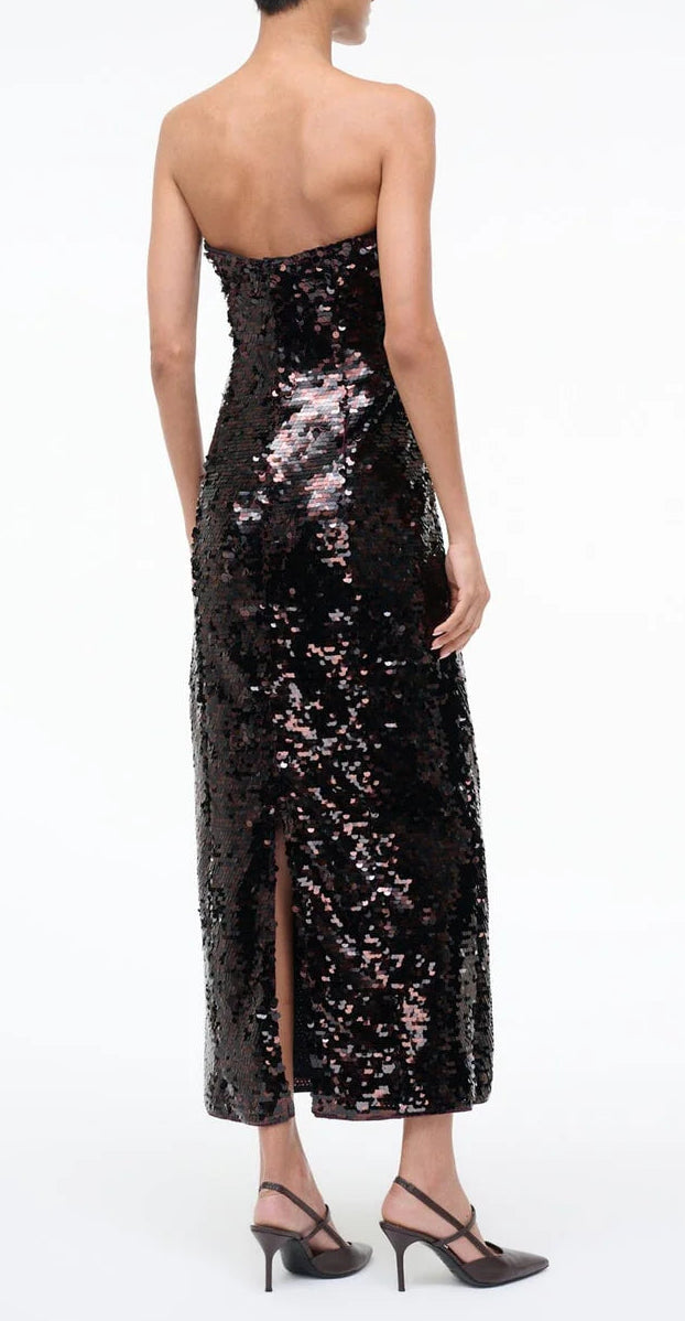 A person wearing the strapless, sequined Staud Cece Dress with a back slit and black high heels stands against a plain white background.