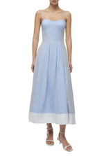A woman wears the Simkhai Chamberlain Cotton Midi Dress in periwinkle multi stripe with a cami neckline and white heeled sandals, standing against a plain white background.