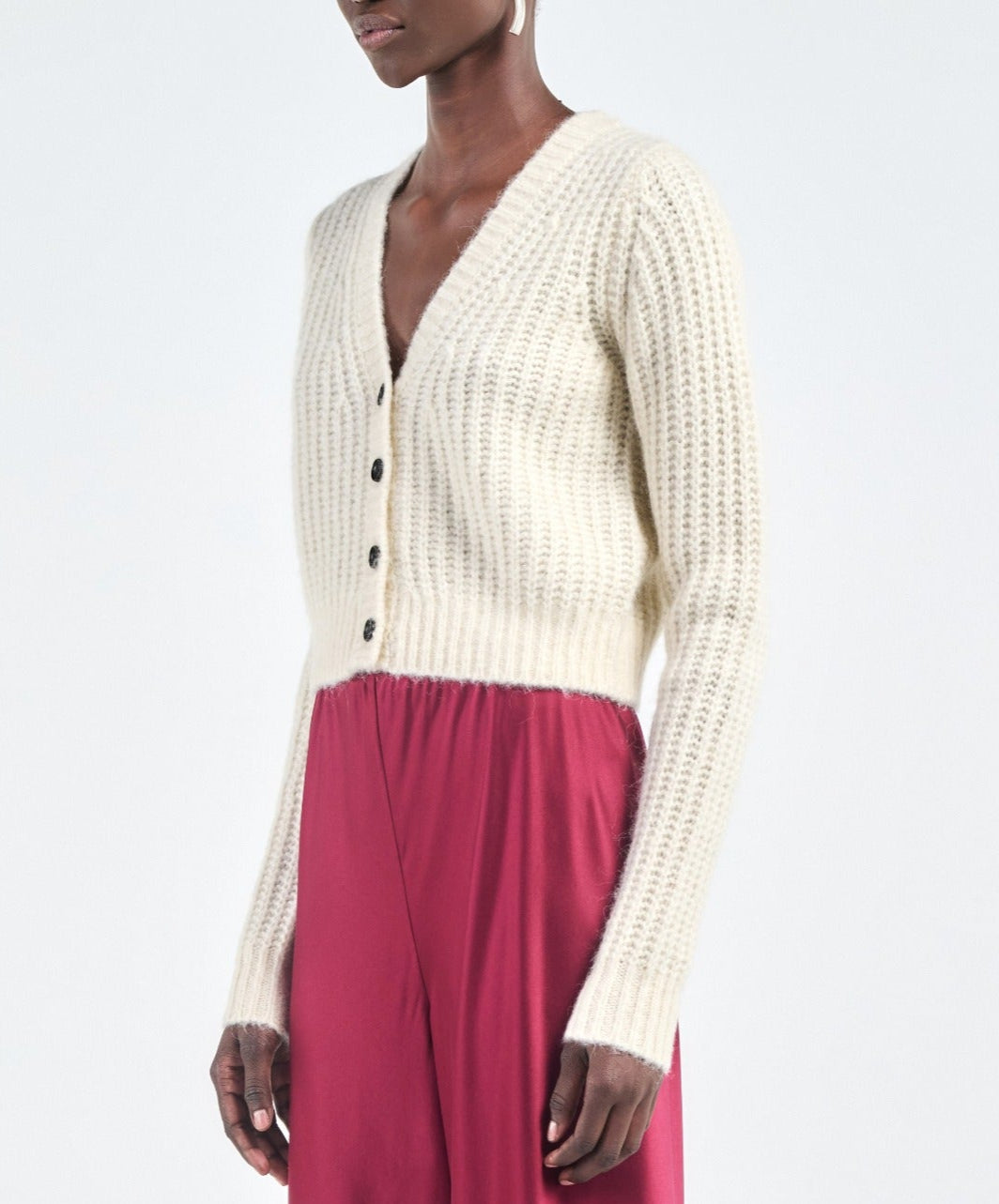 A person wearing the Maria McManus Shrunken V Cardigan—a cream, ribbed, cropped V-neck long-sleeve—paired with a high-waisted red skirt.