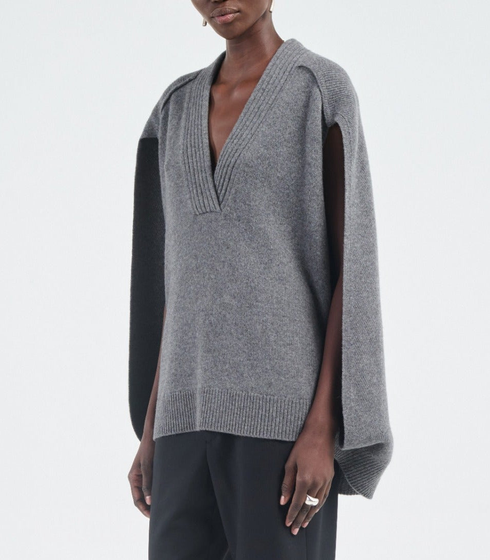 A person wears the Maria McManus Cocoon Cape, a gray V-neck alpaca-wool blend vest with wide arm openings, paired with black pants, against a plain background.