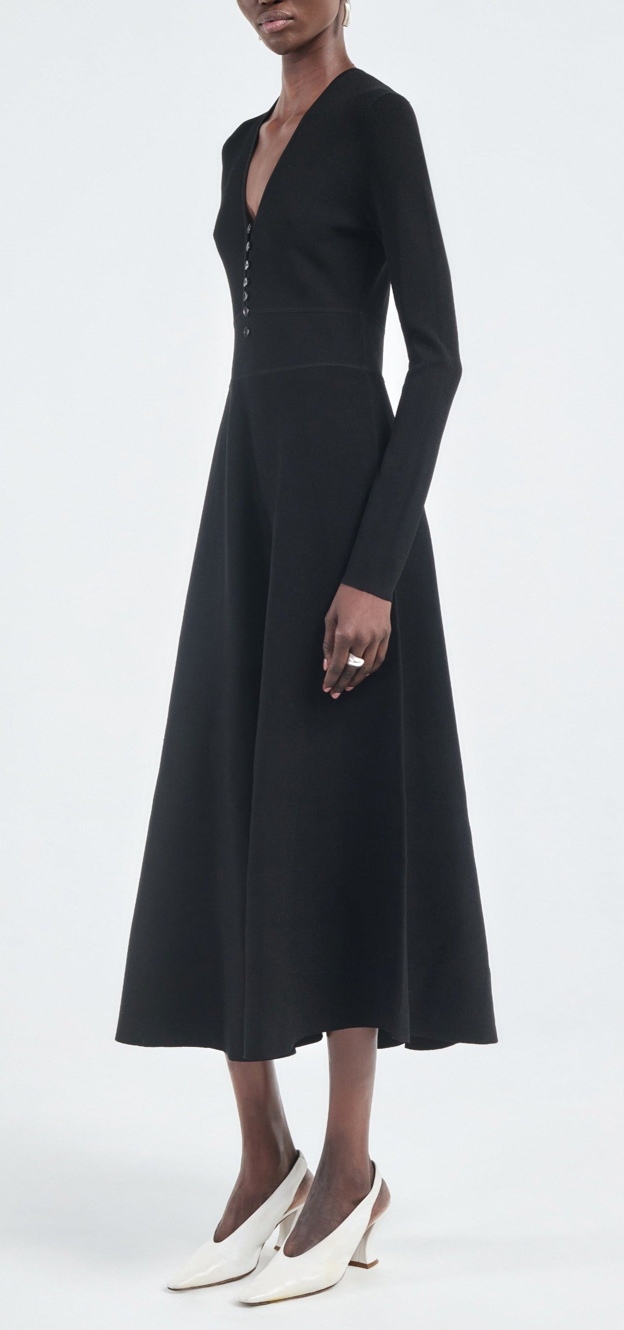A person in the Maria McManus Button Front Dress, made from FSC-certified viscose with corozo nut buttons, and white heeled shoes stands against a plain light background.