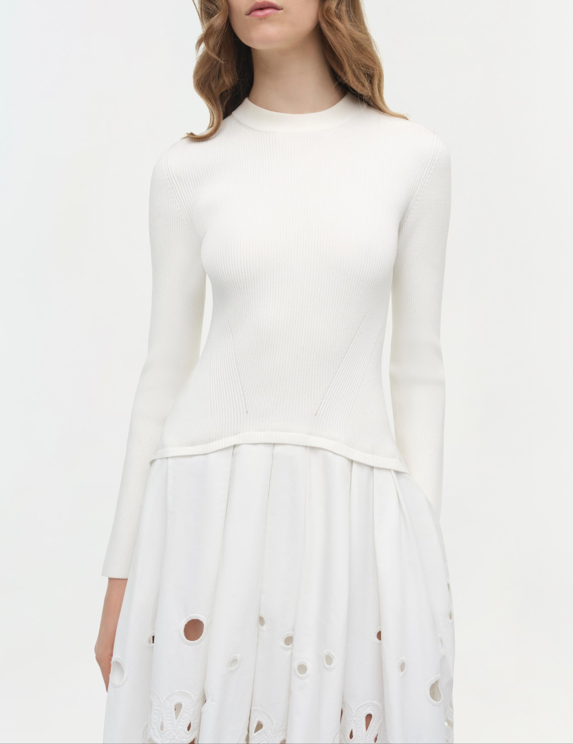 A woman wears the Simkhai Daila Dress, featuring eyelet-embroidered cotton with circular cutouts and long sleeves, standing against a plain light background.