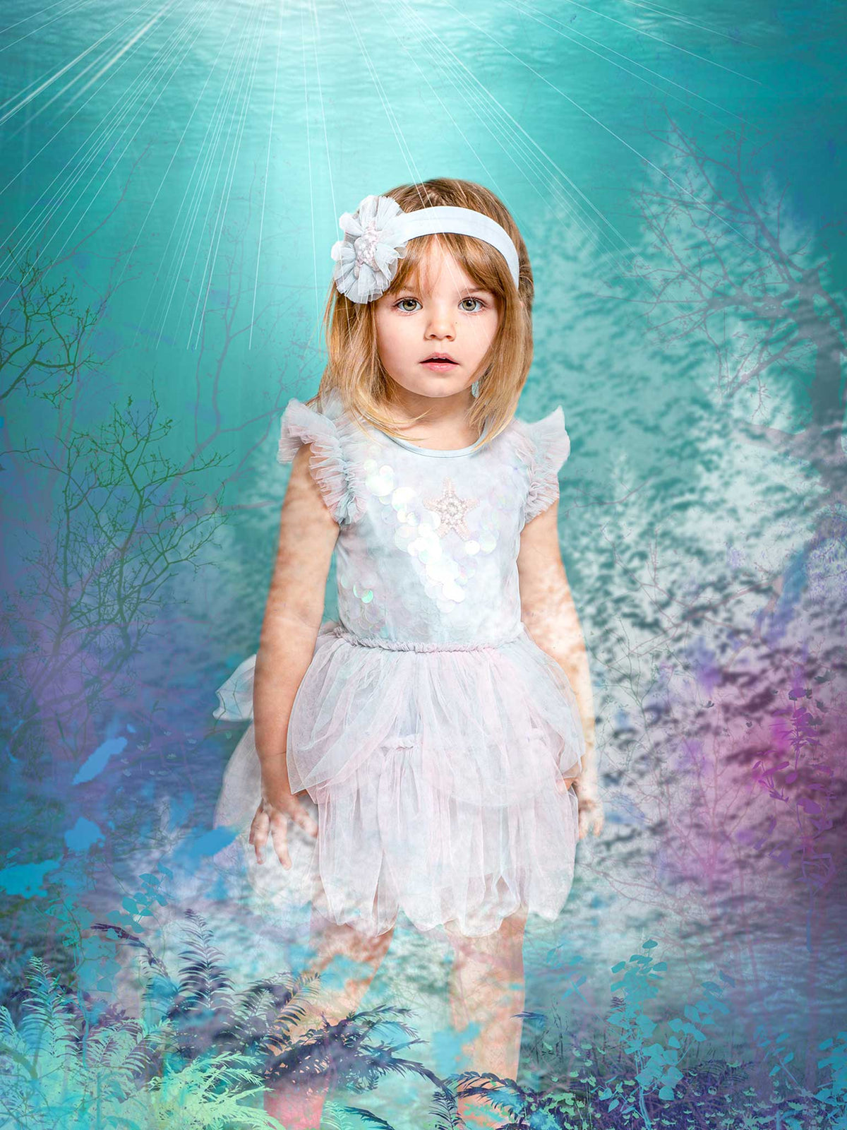 A young girl wearing the Tutu du Monde Baby Girls’ Bebe Mermaid Magic Tutu Dress stands in a dreamy blue and purple fantasy forest illuminated by soft light rays overhead. Delicate starfish motifs shimmer on the skirt, while a dainty headband completes her enchanting look.