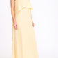 A woman wears the Staud Valencia Linen Dress, a sleeveless light yellow dress with adjustable straps, paired with black strappy sandals, against a plain white background.