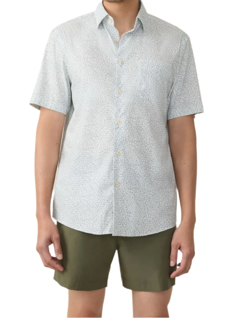 Wearing a Faherty Short-Sleeve Movement™ Monterey Shirt, person stands against a plain white background in an olive green shorts ensemble. The shirt is light-patterned and made from wrinkle-resistant Supima cotton.