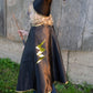 A child dressed in the Great Pretenders Reversible Wizard Cape & Hat stands on grass facing a wooden wall, holding a wand. The outfit features a classic wizard hat and a reversible cape for the perfect spellbinding look.