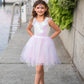 A young girl wears the Great Pretenders Girls' Dreamy Unicorn Dress, barefoot on a waterside walkway with boats and greenery in the background, hands on hips.