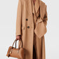 A person in a long camel coat over a matching suit holds the Stella McCartney Ryder Shoulder Bag—a chic, cruelty-free accessory—against a plain background.