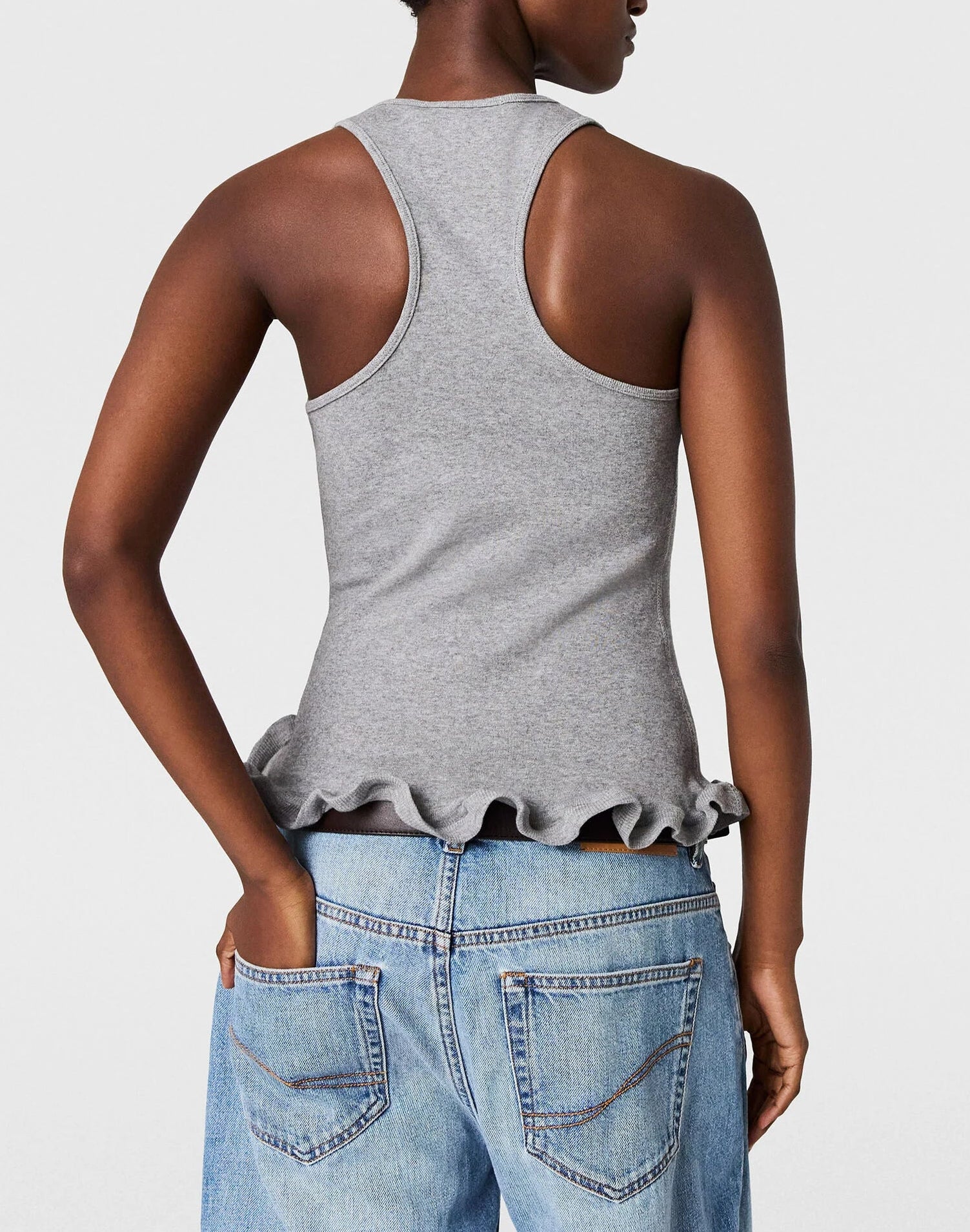 A person shown from the back wears the Stella McCartney Frilled Hem Rib Tank in gray, made from organic cotton, featuring a ribbed texture and frilled hem, paired with blue jeans.