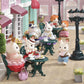 Calico Critters from the Tea and Treats Set gather at outdoor café tables furnished with delightful miniature furniture, sipping tea and enjoying pastries surrounded by charming tea party accessories, while other figures stroll or stand nearby on the cobblestone street.