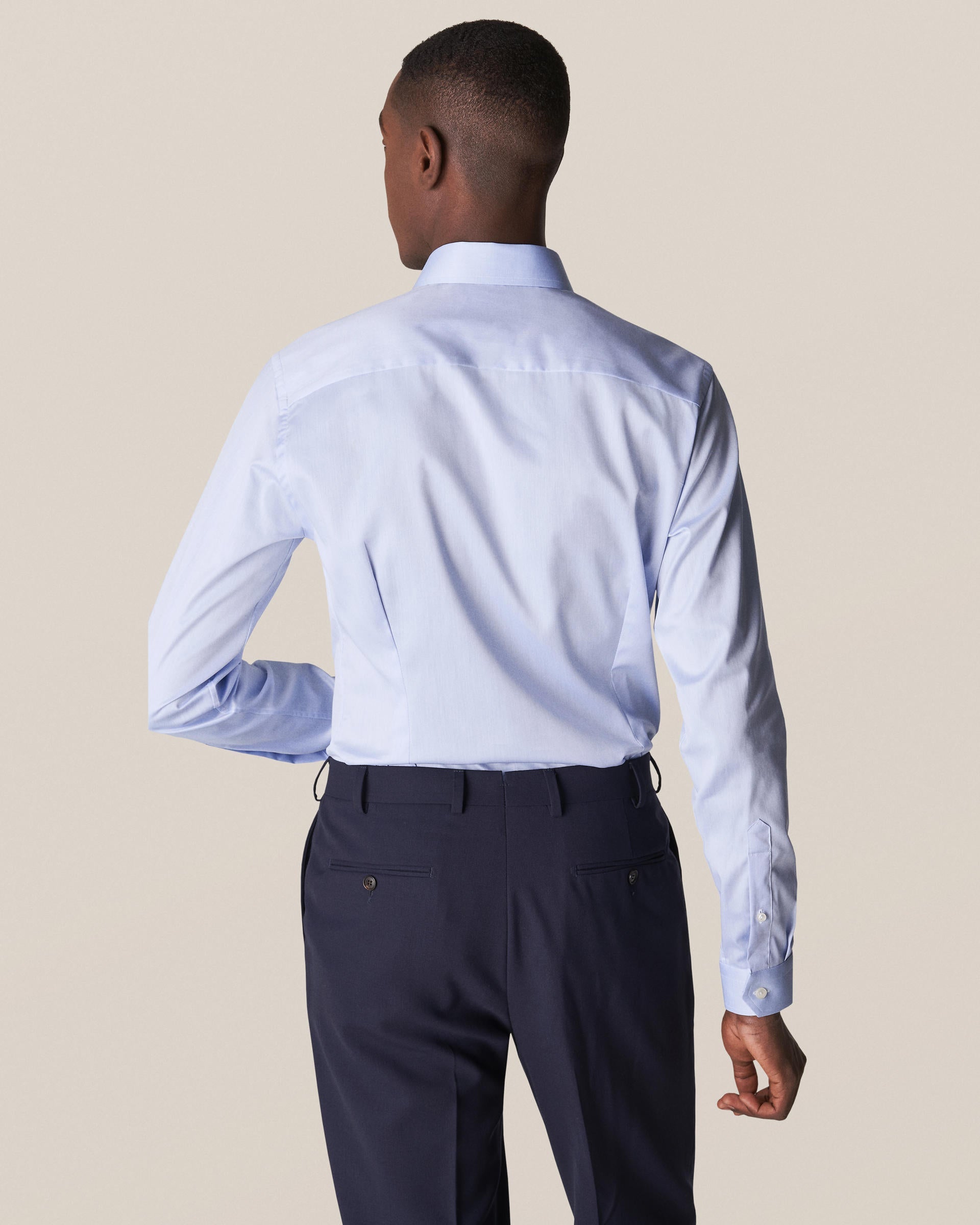 With their back turned and a hand on their hip, a person confidently wears an Eton Light Blue Signature Twill Shirt in Slim Fit. The dark trousers enhance the sleek, wrinkle-free appearance of the ensemble.