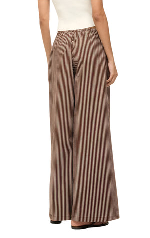 A person wearing a white top and Staud Bonfire Pant, featuring brown striped cotton poplin wide-leg design, stands casually with their back to the camera.