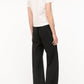 A person stands facing away, wearing a short-sleeve white t-shirt and the Staud Stroll Pant—loose black straight-leg pants with an elastic waistband—against a plain white background.