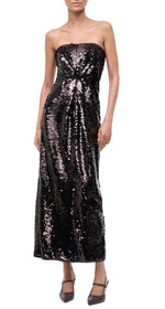 A woman wears a sequined, floor-length black Cece Dress by Staud with dark high heels.