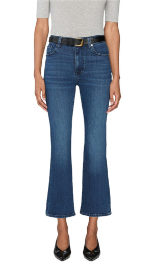 A person wears The Reboot Crop blue bootcut jeans by Frame—ultra-stretchy cotton blend with a cropped inseam—styled with a light gray top, black belt, and black pointed-toe shoes, standing against a plain white background.