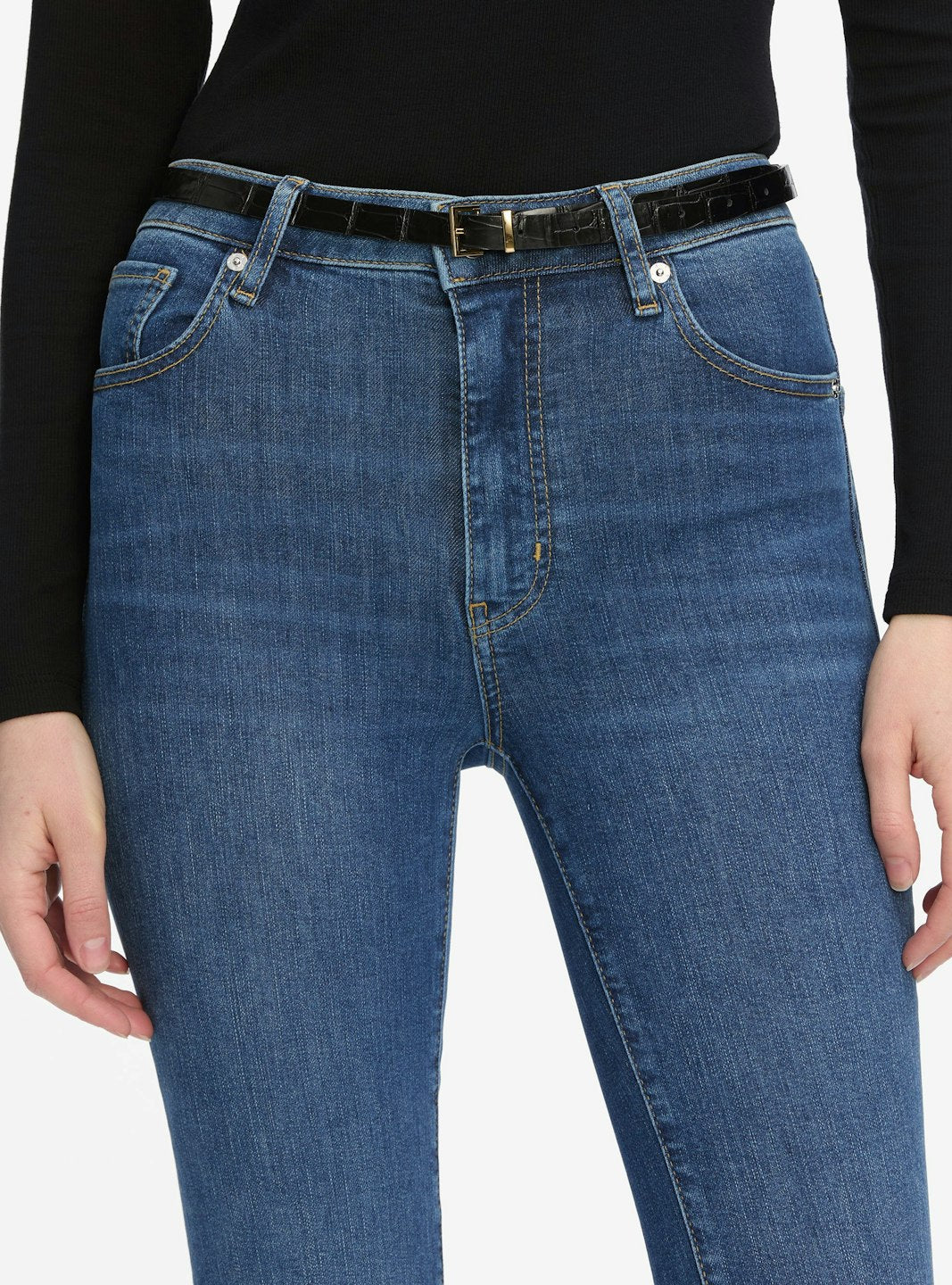 A person wearing Frame's The Reboot Crop high-waisted, ankle-length jeans with a black belt and long-sleeve black top, shown from waist to mid-thigh.