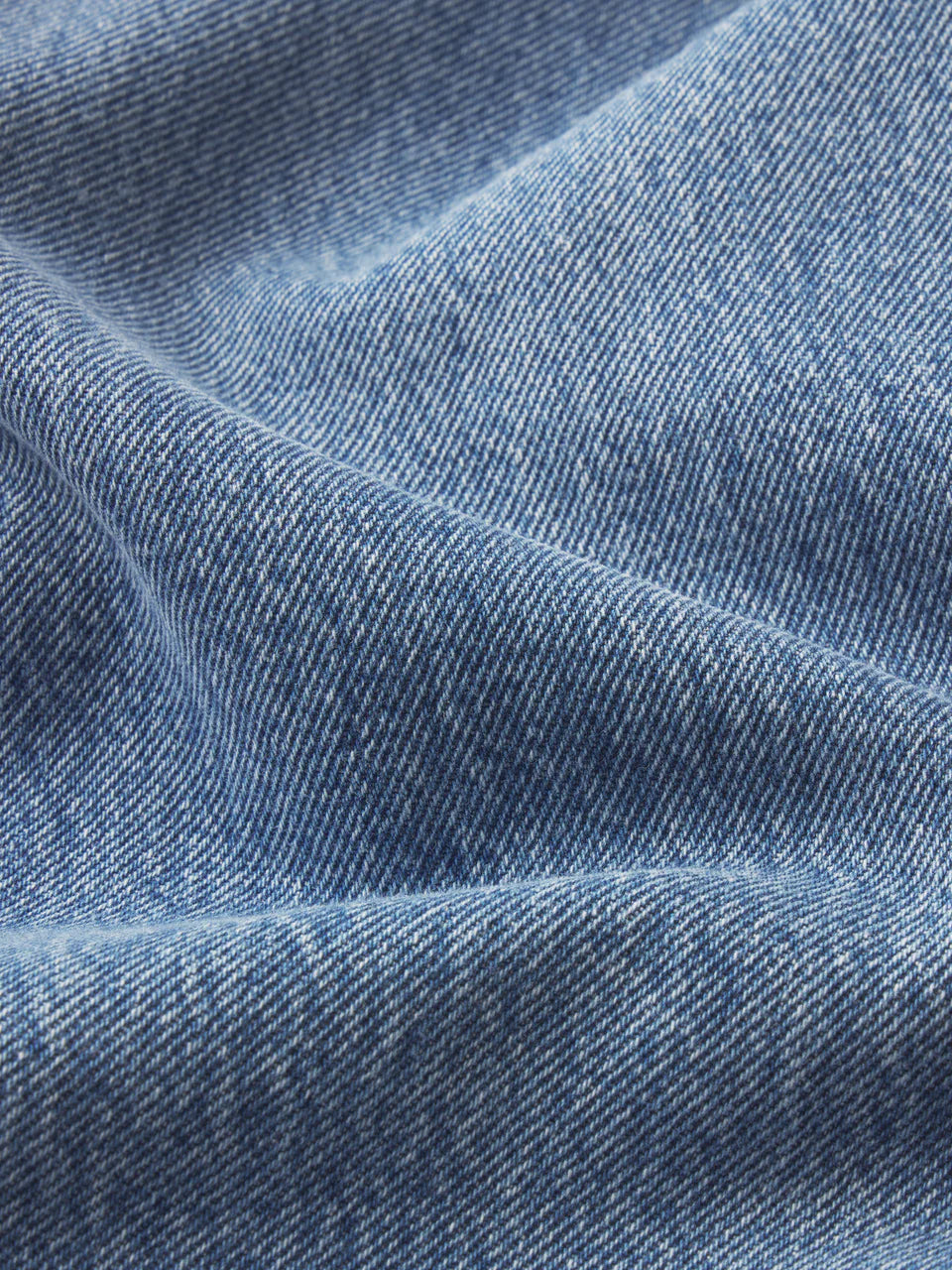 Close-up of light blue denim fabric with diagonal weave and soft folds, evoking a vintage vibe inspired by Frame's The Lax wide-leg flare jeans.