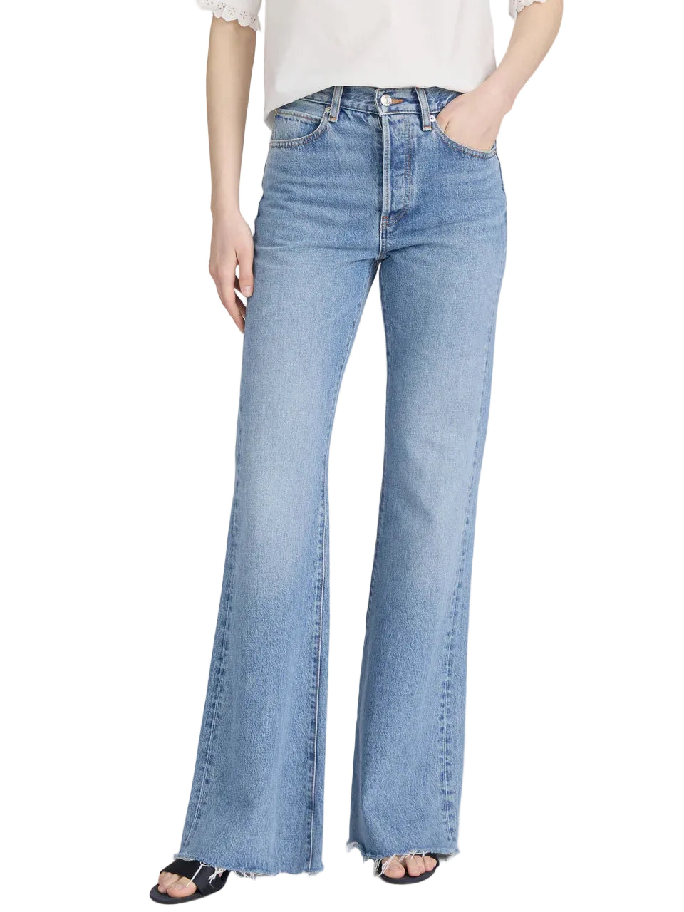 Model wears The Lax jeans by Frame in light blue, featuring a high-waisted, wide-leg flare with raw hems, paired with a white top and black open-toe sandals for a subtle vintage touch against a plain background.