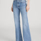 A person wearing Frame's The Lax rigid denim jeans—light blue, high-waisted, wide-leg flare style with frayed hems—paired with a white short-sleeve top and black sandals, stands against a plain background for a vintage vibe.