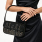 A woman in a black satin dress holds the Staud Tommy Beaded Bag, a vegan leather handbag adorned with a gold city skyline design.