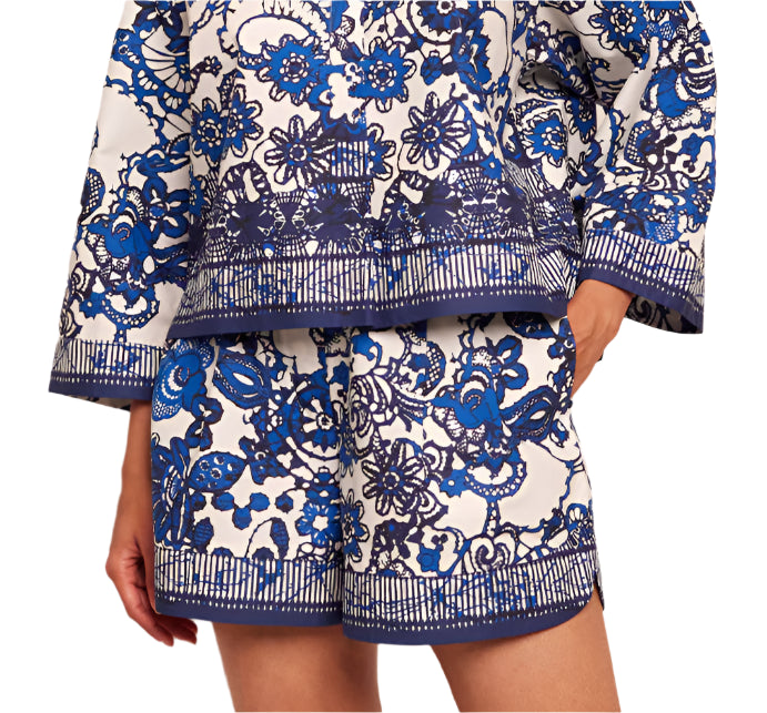 A person wearing Cara Cara's white outfit with a blue intricate floral pattern, featuring a long-sleeve top and matching Trish Shorts by Cara Cara with an elastic waistband.