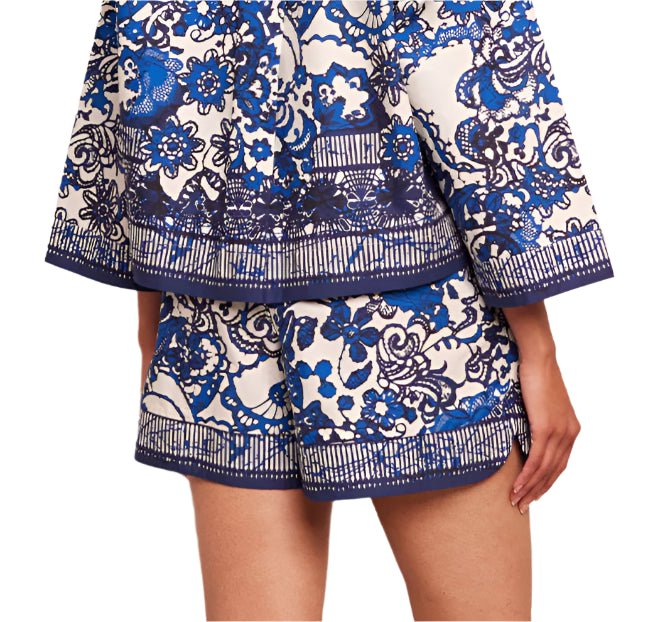 The Cara Cara Trish Shorts, styled in a blue and white floral pattern and featuring an elastic waistband, are paired with a matching long-sleeved top. The ensemble is both stylish and functional, with discreetly integrated pockets enhancing the outfit's appeal.