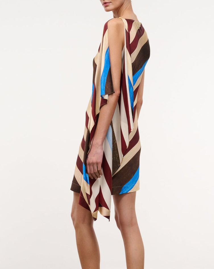 A person wearing the Staud Sabina Silk Dress, featuring an easy-fit column silhouette with a sleeveless, knee-length asymmetrical design and diagonal stripes in brown, beige, red, and blue, shown from the side against a plain background.