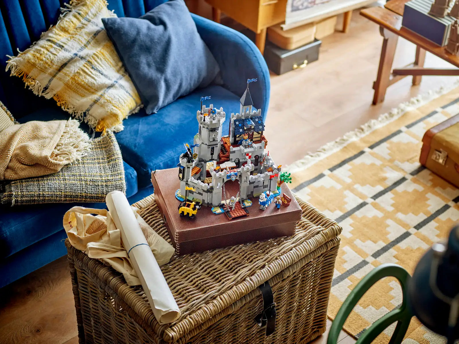 The LEGO® Creator™ 3-in-1 Medieval Horse Knight Castle by Legos - Toyhouse sits atop a closed book on a wicker basket, with a sofa and patterned rug in the living room background.