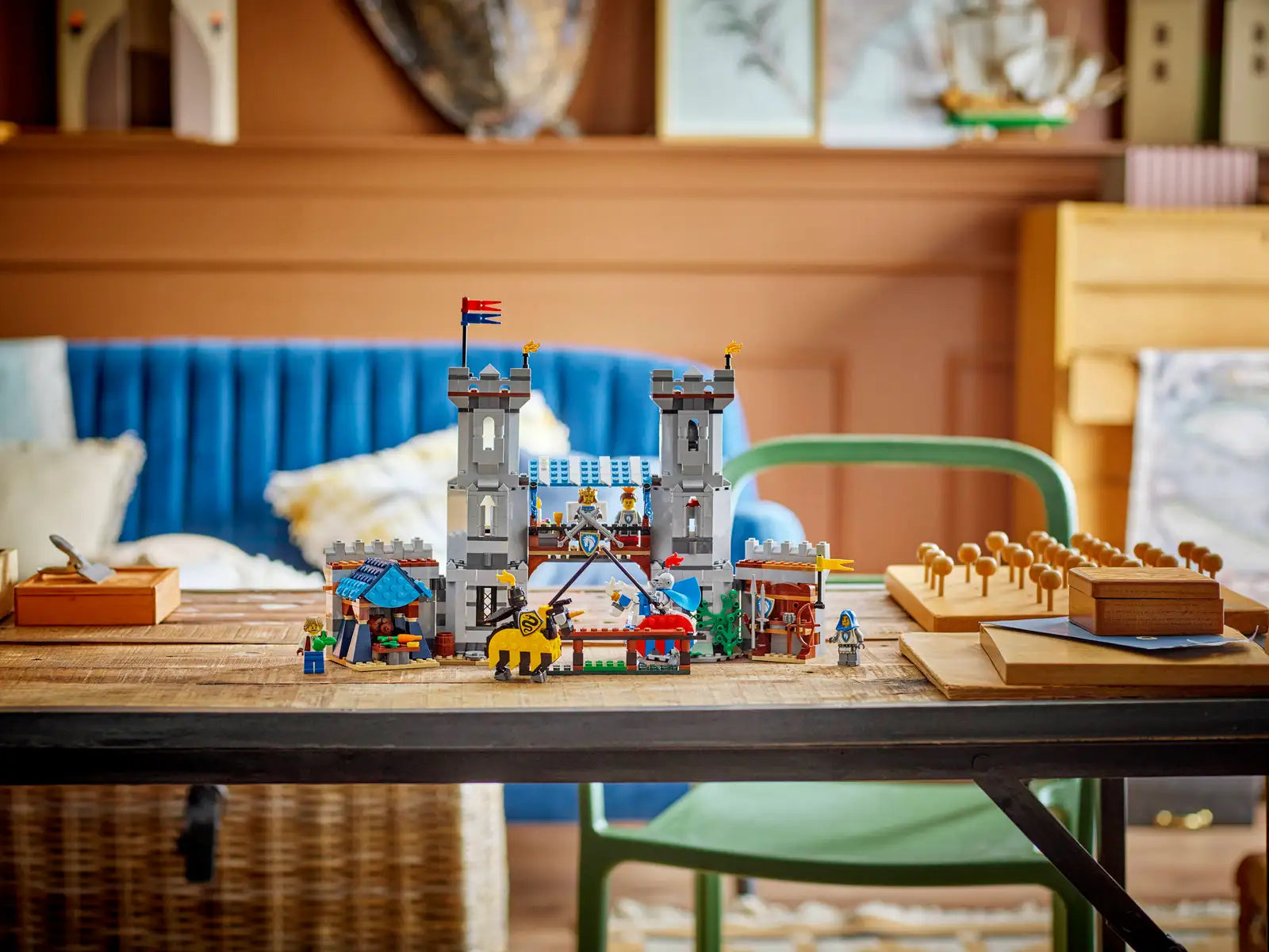 The Legos - Toyhouse LEGO® Creator™ 3-in-1 Medieval Horse Knight Castle set with figures and stalls is displayed on a wooden table in a cozy living room, featuring a blue sofa and decorative accents in the background.