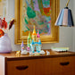 The LEGO® Creator™ 3-in-1 Unicorn Castle by Legos - Toyhouse, featuring animal figures and a unicorn toy, sits on a wooden dresser beside a pastel flower vase, underneath a framed abstract painting and a lamp.
