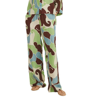 Wearing the Cara Cara Girona Pant, featuring a flowy wide-leg silhouette and an abstract swirl pattern in green, blue, brown, and cream with an adjustable tie waist, styled with sandals.