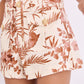 Someone dressed in Cara Cara's Xenia Short, featuring a high-waisted mini cut with a bold brown floral and leaf print and decorative pocket buttons.
