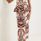 A woman wearing the Cara Cara Sienna Skirt, a bold pink, brown, and cream patterned midi with peplum waist, paired with a strapless fitted top and white heeled sandals.